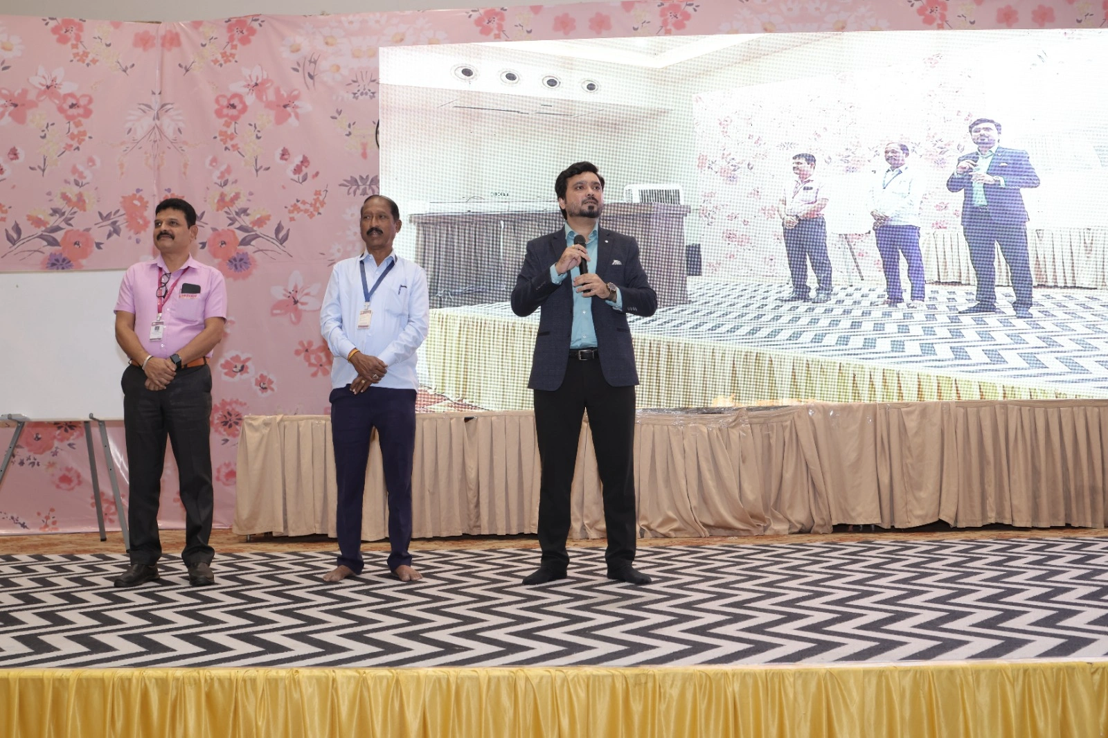 Avinash Chate with a microphone on stage alongside two Shivpratap Co-operative Credit Society participants during an on-stage exercise, Karad
