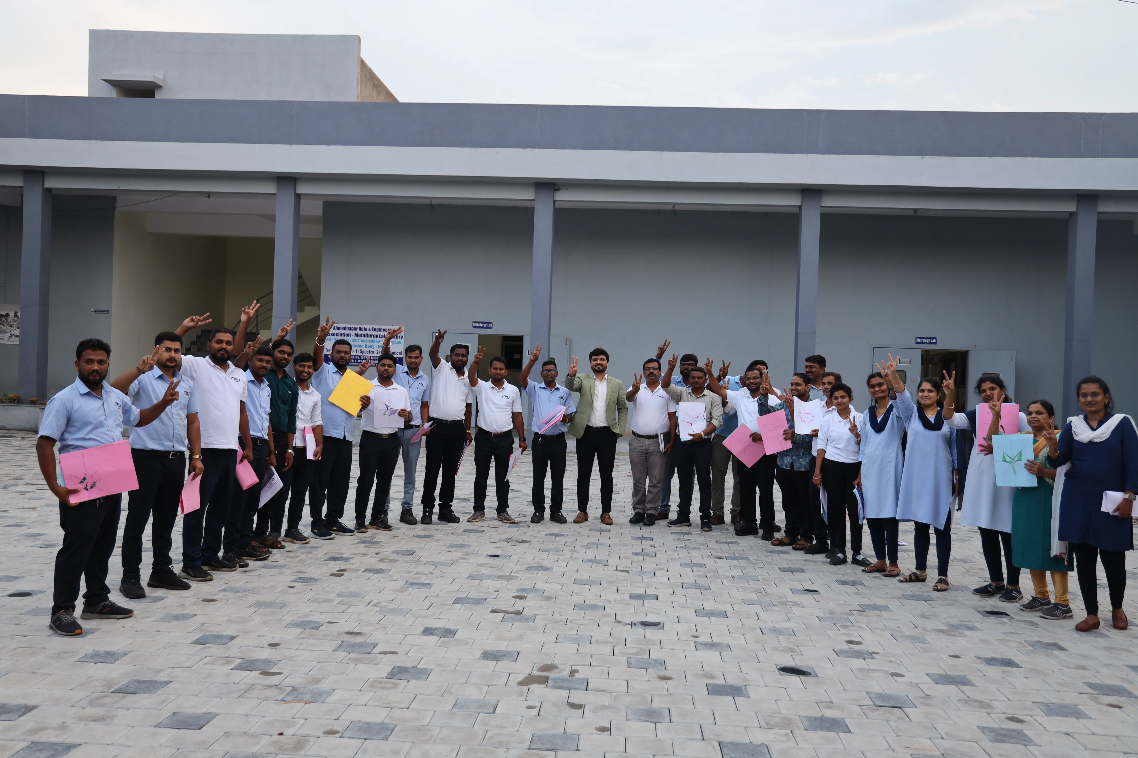 JM Aluext Profiles employees in uniform shirts lined up outdoors with Avinash Chate, holding up the paper kites they made during the Becoming a Star programme, Ahmednagar