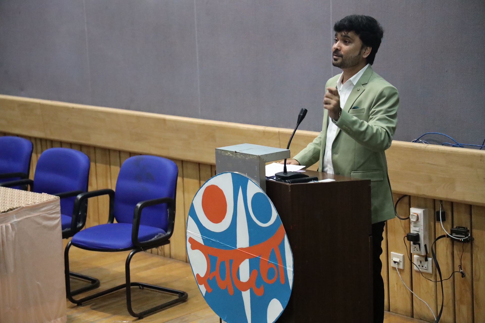 Avinash Chate speaking from the auditorium podium at the College of Engineering Pune student seminar, beside the Marathi “Spandan” event board