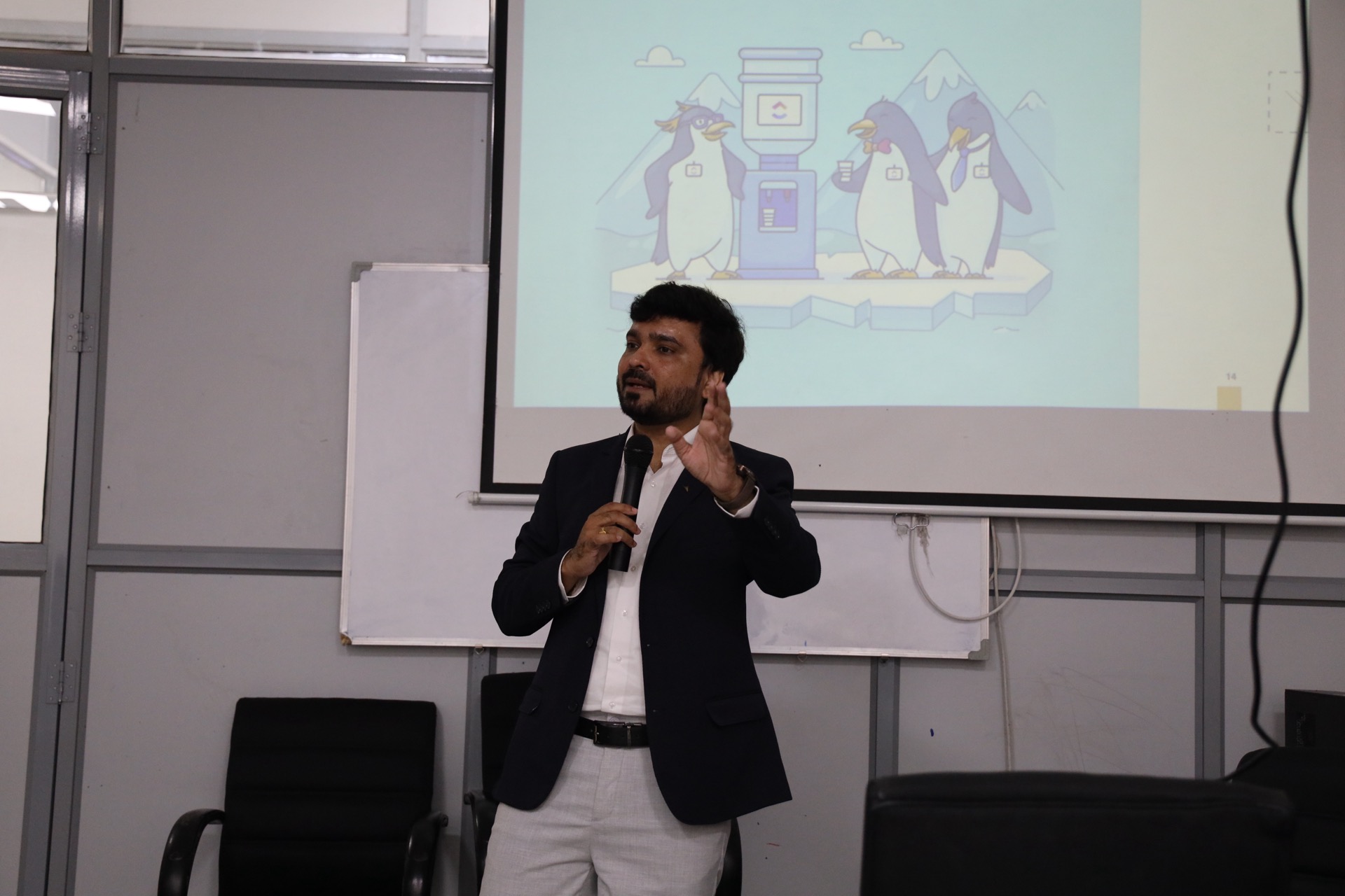 Avinash Chate with a microphone speaking in the training room during the emotional-intelligence session for JM Aluext Profiles, a cartoon illustration projected behind him