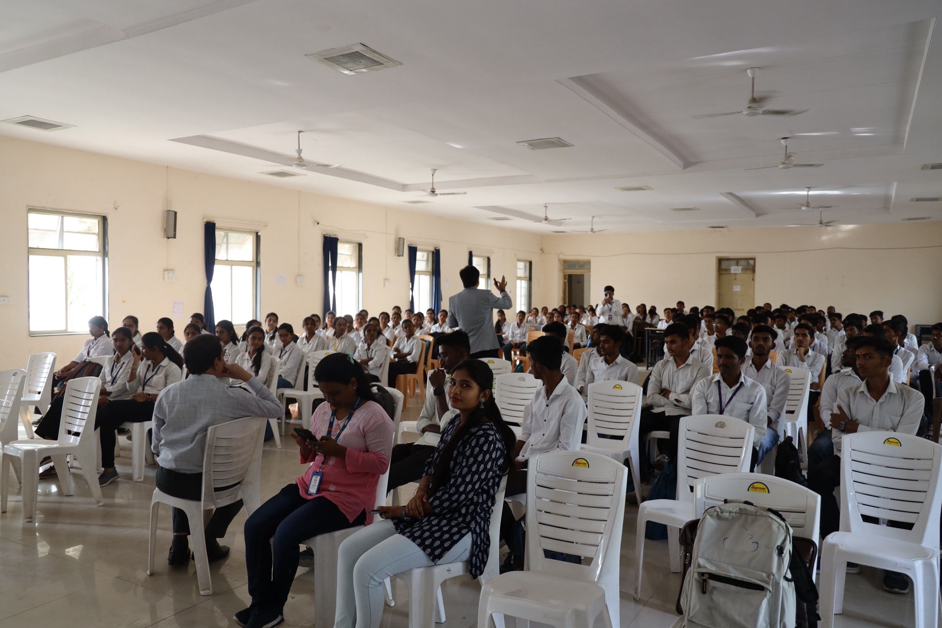 A packed hall of Government Polytechnic students in white uniforms with Avinash Chate speaking mid-audience, Chhatrapati Sambhajinagar