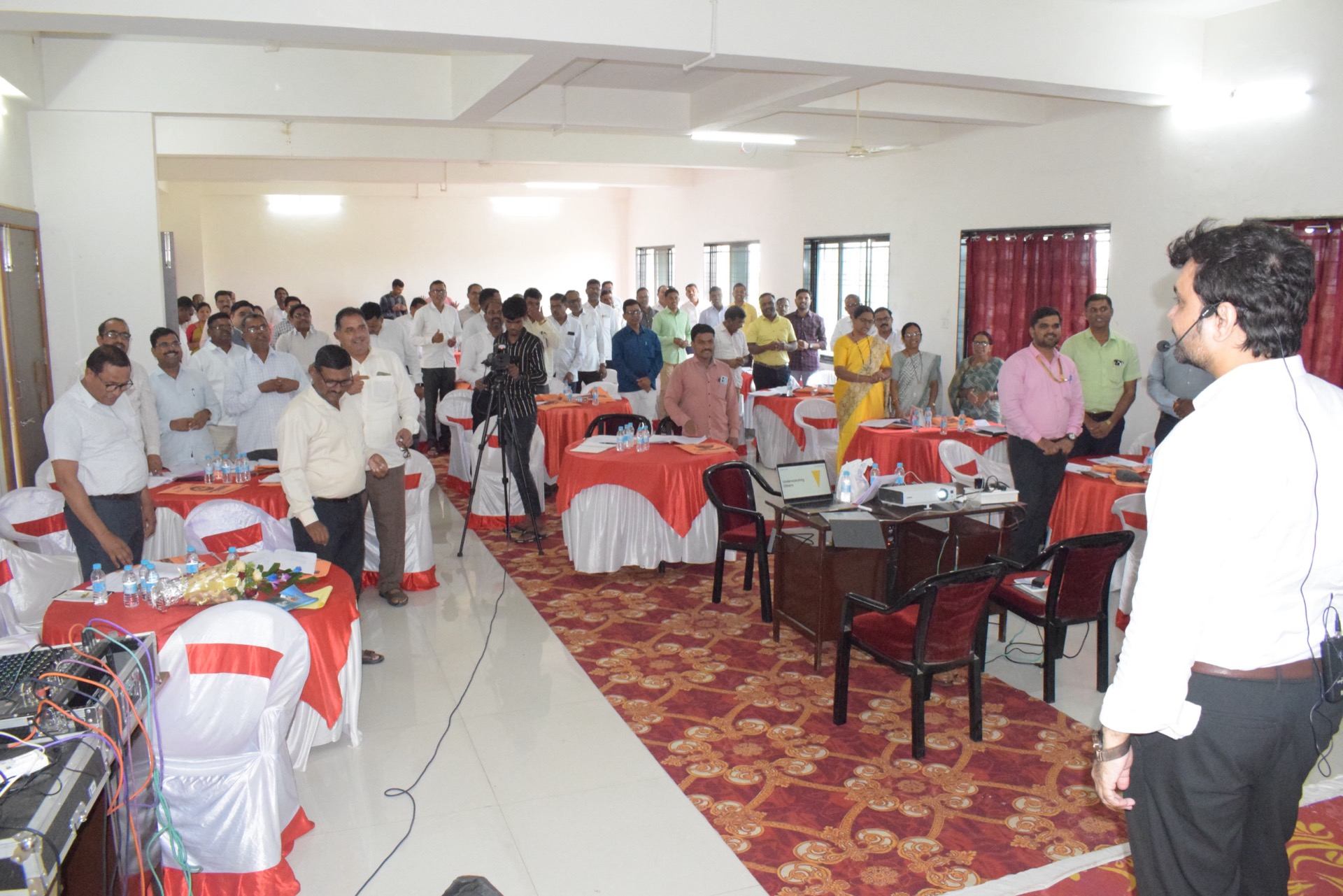 Avinash Chate in a headset microphone addressing Aabasaheb Kakde Educational Group staff standing at round tables during the leadership programme at Shevgaon