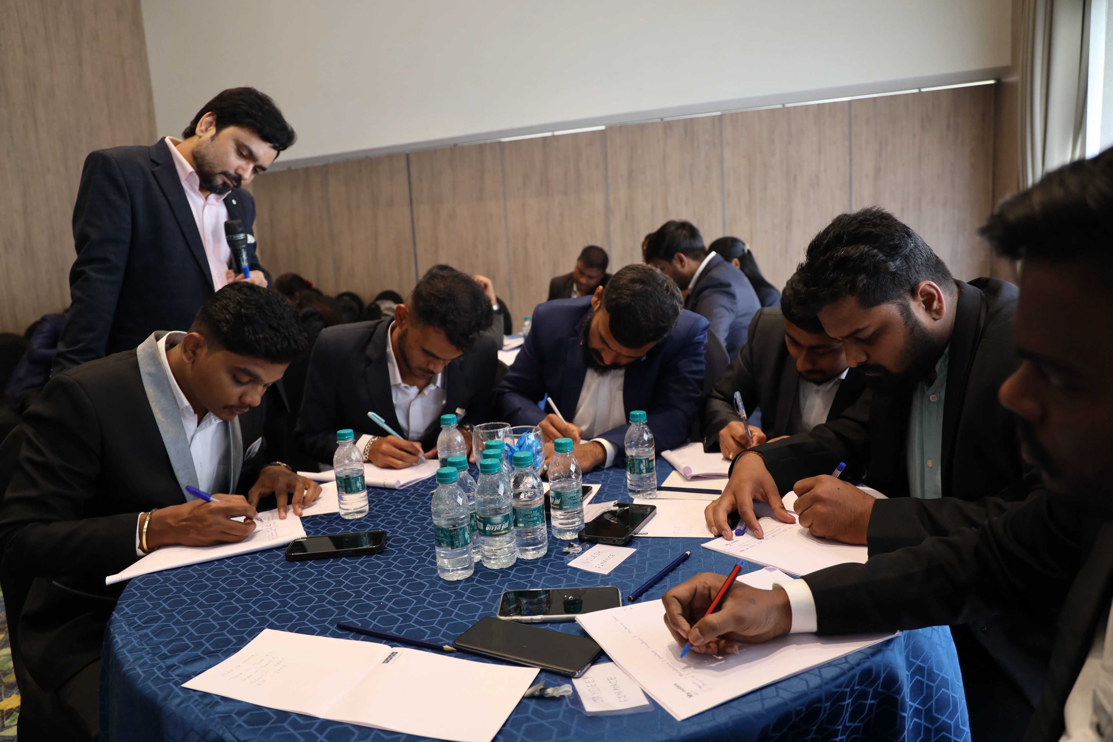 Strong Wings Honda participants writing through a sales exercise at a round table while Avinash Chate stands over the group facilitating, Day 2 at Pimpri-Chinchwad